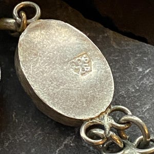 Pode incluir: Close-up de um colar de prata com elos ovais. Os elos t&ecirc;m uma superf&iacute;cie texturizada e s&atilde;o conectados por pequenos conectores ornamentados. Uma pequena marca de contraste &eacute; vis&iacute;vel em um dos elos.