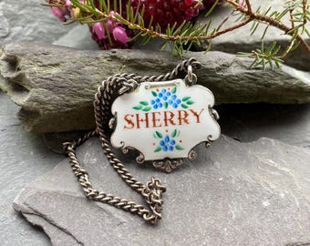 May include: A silver chain with a porcelain bottle tag that says "SHERRY" in orange lettering. The tag is decorated with blue and green floral designs.