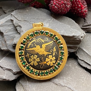May include: Gold pendant with a black enamel background and a gold bird design. The pendant is surrounded by a circle of green rhinestones.