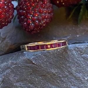 May include: A gold band ring with a row of small, square-shaped ruby stones set in the band.