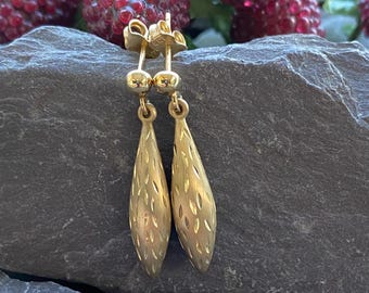 May include: A pair of gold drop earrings with a textured, diamond-shaped design. The earrings are made of 14k gold.