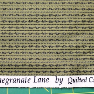 May include: A woven fabric featuring an olive green background with repeating horizontal rows of thin black lines and small, dark, leaf-like motifs. The white selvage edge displays the printed text Pomegranate Lane by Quilted Crow Girls.