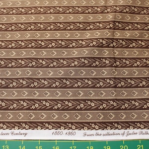 Op de afbeelding: Bruine en beige stof met een herhalend patroon van horizontale strepen. De strepen wisselen af tussen effen bruine en beige diamant- en bloemmotieven. De stof heeft de tekst "Nineteen Century 1850-1860 From the collection of Judie Rothermel".