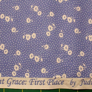 Könnte beinhalten: Blauer Stoff mit weißem Blumen- und Tupfenmuster. Der Stoff hat einen hellblauen Hintergrund mit kleinen weißen Punkten und weißen Blumengruppen. Der Text "Aunt Grace: First Place by Judie Rother" ist unten aufgedruckt.
