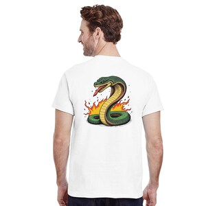 Könnte beinhalten: Weißes T-Shirt mit einer detaillierten Illustration einer grünen Kobra mit roter Zunge, umgeben von Flammen. Das Schlangen-Design befindet sich auf der Rückseite des Shirts. Das Shirt besteht aus einem weichen, bequemen Material.