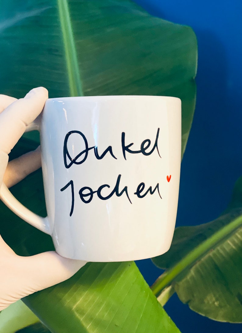 May include: White ceramic mug with black cursive writing that says "Onkel Jochen" with a small red heart.