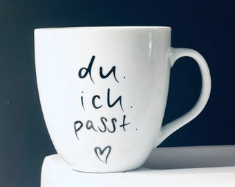 May include: White ceramic mug with black handwritten text that reads "du. ich. passt." and a small heart.