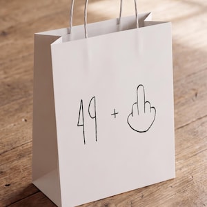 May include: A white paper gift bag with two twisted paper handles. The front of the bag features a black hand-drawn graphic consisting of the number 49, a plus sign, and an illustration of a hand making a middle finger gesture.