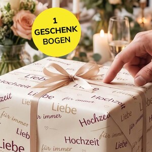 Könnte beinhalten: Eine quadratische Geschenkbox, eingewickelt in cremefarbenes Papier mit dem wiederholten deutschen Text "Liebe", "Hochzeit" und "für immer" in dunkelbrauner Schrift, verziert mit einer hellbeigen Satinschleife oben.