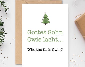 May include: A white Christmas card with a green Christmas tree illustration and text in German and English. The German text reads "Gottes Sohn Owie lacht..." and the English text reads "Who the f... is Owie?" The card is paired with a brown envelope.