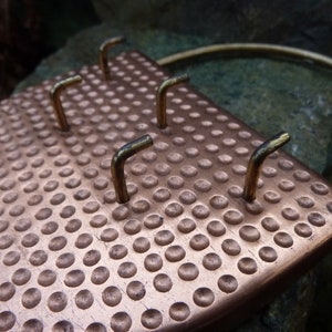 Peut inclure: Un porte-clés en cuivre avec une texture martelée et cinq crochets en laiton. Le porte-clés a un anneau en laiton sur le dessus pour l'accrocher.