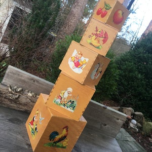 May include: A stack of wooden blocks with colorful illustrations of animals, a child, fruit, and a rooster. The blocks are painted in shades of brown and yellow.