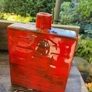 Peut inclure: Un vase en céramique rouge avec un corps carré et un col étroit. Le vase a une surface texturée et une finition brillante.