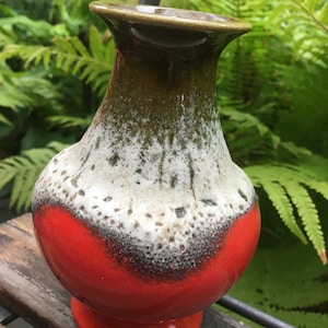 Pode incluir: Um vaso de cerâmica vermelho, branco e verde com um esmalte salpicado. O vaso tem um corpo arredondado e uma borda alargada.