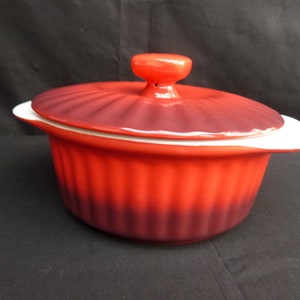 Può includere: Piatto da forno in ceramica rosso e bianco con coperchio. Il piatto ha un design scanalato e un gradiente di rosso a viola.