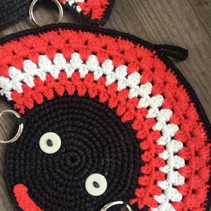 Op de afbeelding: Twee gebreide zwarte, rode en witte ovenwanten met een glimlachend gezicht en twee sleutelringen.
