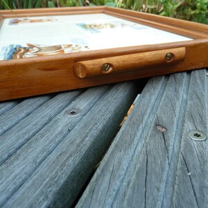 May include: A wooden tray with a white tile insert and a brass handle. The tray is resting on a gray wooden surface.