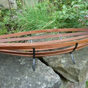 Op de afbeelding: Een houten fruitschaal met een gebogen vorm en zwarte metalen poten. De schaal is gemaakt van dunne stroken hout en heeft een natuurlijke houtkleur.