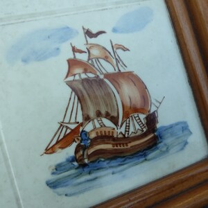 May include: A framed tile with a hand-painted image of a brown and white sailing ship with blue and white waves. The ship has brown sails and a blue and white flag.