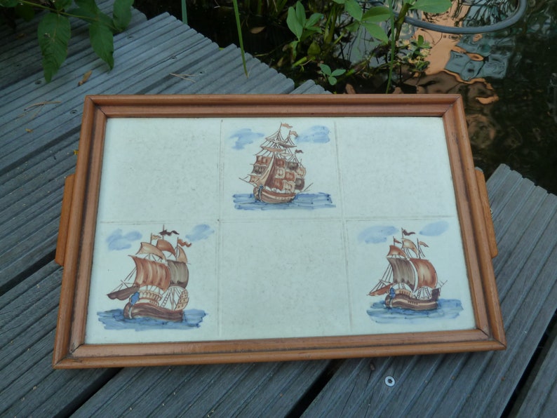 May include: A wooden serving tray with four square tiles featuring hand-painted images of sailing ships. The tiles are surrounded by a wooden frame.