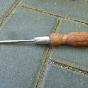 Könnte beinhalten: Ein Schraubendreher mit Holzgriff und einem Metallenschaft. Der Schraubendreher liegt auf einer grauen Betonfläche.