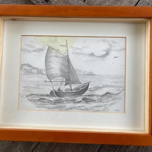 Könnte beinhalten: Eine gerahmte Bleistiftzeichnung eines Segelboots mit einem einzigen Segel auf einem Gewässer. Das Segelboot befindet sich im Vordergrund des Bildes und das Wasser im Hintergrund. Die Zeichnung ist in Grautönen und Weiß gehalten.