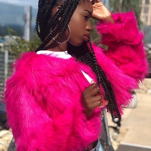 May include: A pink faux fur jacket with long sleeves. The jacket is cropped and has a relaxed fit.
