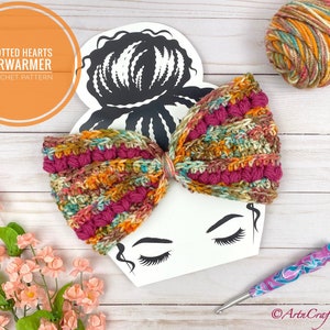 May include: A crochet ear warmer with a knotted heart design in shades of pink, orange, brown, and green. The ear warmer is displayed on a white background with a drawing of a woman's face. The yarn used to make the ear warmer is shown in a ball to the right of the ear warmer.