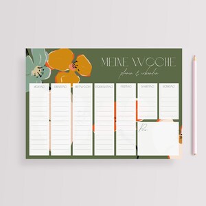 May include: A green weekly planner with a floral design featuring orange, yellow, and green flowers. The planner has columns for each day of the week, labeled in German: Montag, Dienstag, Mittwoch, Donnerstag, Freitag, Samstag, Sonntag. The text "Meine Woche plan & erleb" is at the top of the planner.