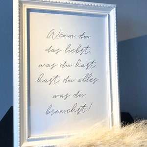 Könnte beinhalten: Weißer gerahmter Druck mit dem Text "Wenn du das liebst. was du hast. hast du alles. was du brauchst!" in schwarzer kursivschrift.