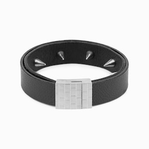 Puede incluir: Un brazalete de cuero negro con tachuelas plateadas y un cierre de hebilla plateada.