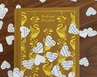 May include: A yellow and brown book with the title "Pride and Prejudice" on the cover. The book is surrounded by white paper hearts with text from the book printed on them.