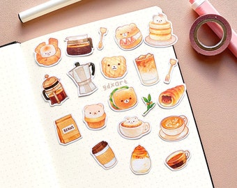 May include: A set of 17 stickers featuring cute illustrations of coffee, pastries, and bears. The stickers are on a white background with a light brown notebook in the background.