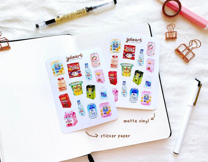 May include: Two sheets of stickers featuring illustrations of various Japanese snacks and drinks. The stickers are on a white background with the text "ydxart sticker sheets" printed on each sheet. The text "matte vinyl" is written on the right sheet and "sticker paper" is written on the left sheet.