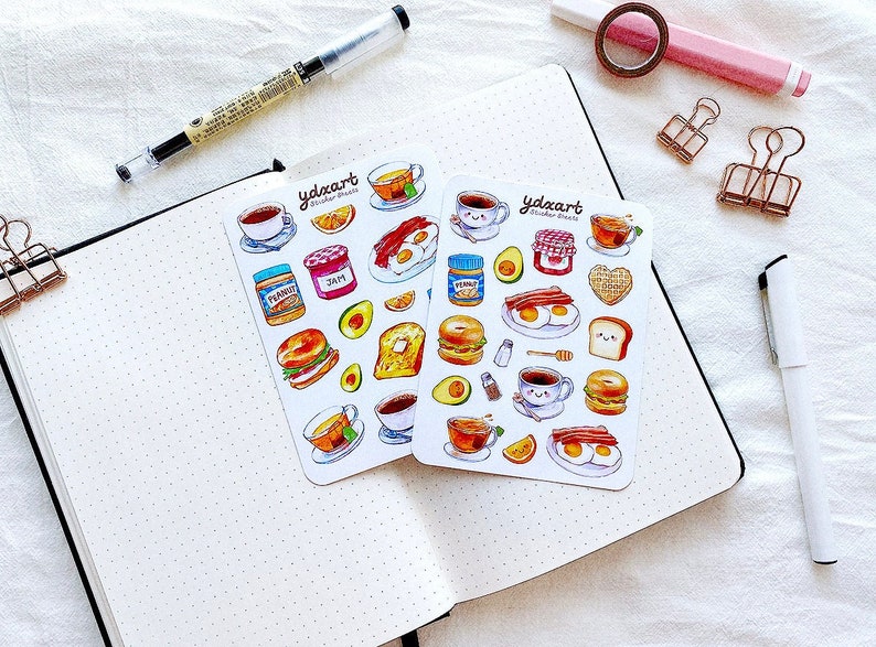 May include: Two sheets of stickers featuring illustrations of breakfast foods, including eggs, bacon, toast, coffee, and avocado. The stickers are white with a black border and the text "ydaart Studio Goods" in black.