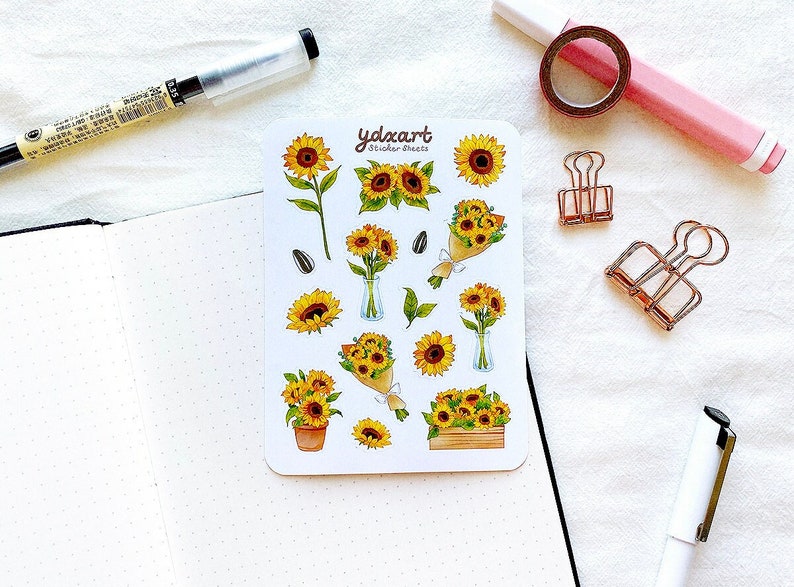 Peut inclure: Une feuille d'autocollants de tournesols avec une vari&eacute;t&eacute; de motifs, y compris des tournesols simples, des bouquets et des tournesols en pot. La feuille d'autocollants est blanche avec le texte "ydexart sticker sheets" imprim&eacute; en noir.