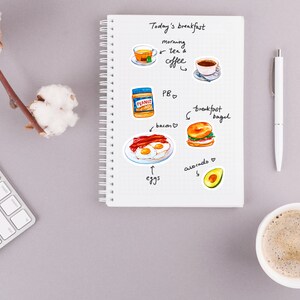 May include: A white notebook with a spiral binding, open to a page with a handwritten list of breakfast items. The list includes "Today's breakfast", "morning tea & coffee", "PB", "bacon", "eggs", "breakfast bagel", and "avocado". There are hand-drawn illustrations of each item.