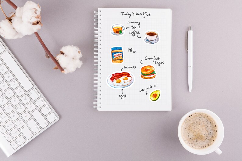 May include: A white notebook with a spiral binding, open to a page with a handwritten list of breakfast items. The list includes "Today's breakfast", "morning tea & coffee", "PB", "bacon", "eggs", "breakfast bagel", and "avocado". There are hand-drawn illustrations of each item.