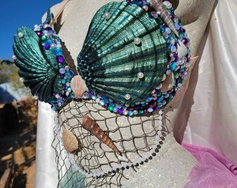 May include: A teal green seashell bra with pearl and jewel embellishments. The bra is decorated with seashells, netting, and a pearl necklace.