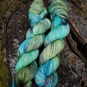 May include: Two skeins of hand-dyed yarn in shades of green, blue, and black. The yarn is twisted and has a variegated color pattern.