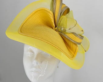 May include: A yellow hat with a large, layered bow made of yellow and gold fabric. The hat is decorated with small gold beads and a large, sparkly, gold-toned embellishment.