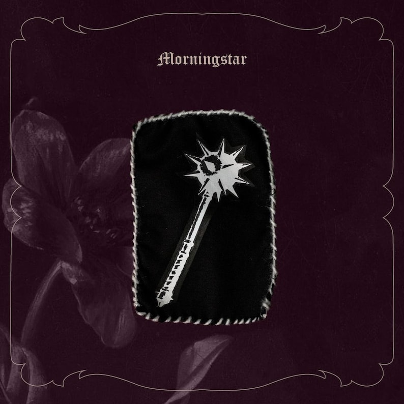 May include: A black patch featuring a white Morningstar weapon design. The patch is edged with white stitching and has the word "Morningstar" above the design. The background is a dark burgundy colour.