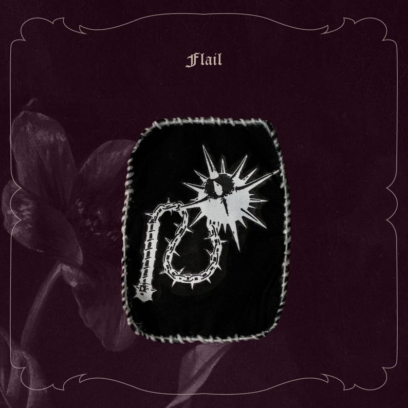 May include: Black patch with a white flail design, featuring a spiked ball and chain. The patch has a white stitched border and the word "Flail" at the top. Set against a dark purple background with floral accents.