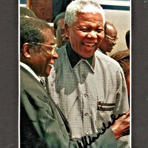 Può includere: Una fotografia in bianco e nero di due uomini che sorridono. L'uomo a sinistra indossa un abito scuro e degli occhiali. L'uomo a destra indossa una camicia a fantasia e ha i capelli bianchi. La foto è firmata "Mandela".