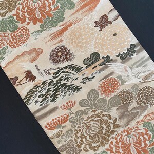 May include: A beige fabric with a repeating pattern of white, brown, and orange flowers. The fabric has a textured, almost embroidered look.