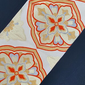 May include: White fabric with a repeating pattern of orange, red, and blue floral designs. The fabric has a subtle shimmer.
