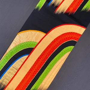 May include: Black fabric with a colourful geometric pattern of curved lines and woven designs in red, green, gold, and blue.