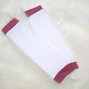 May include: A pair of white arm warmers with a pink trim. The arm warmers are made of a soft, stretchy fabric.
