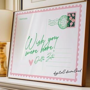 May include: A framed postcard print with a pink border and a green postage stamp featuring pink flowers. The text "Wish you were here!" is written in green script, with "Delta Zeta" below and a pink heart.
