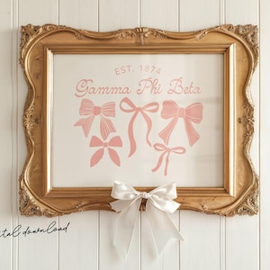 Peut inclure: Une impression encadrée dans un cadre doré orné. L'impression présente des nœuds roses et le texte "EST. 1874 Gamma Phi Beta". Un nœud blanc est attaché au bas du cadre. Les mots "digital download" sont écrits en bas à gauche.